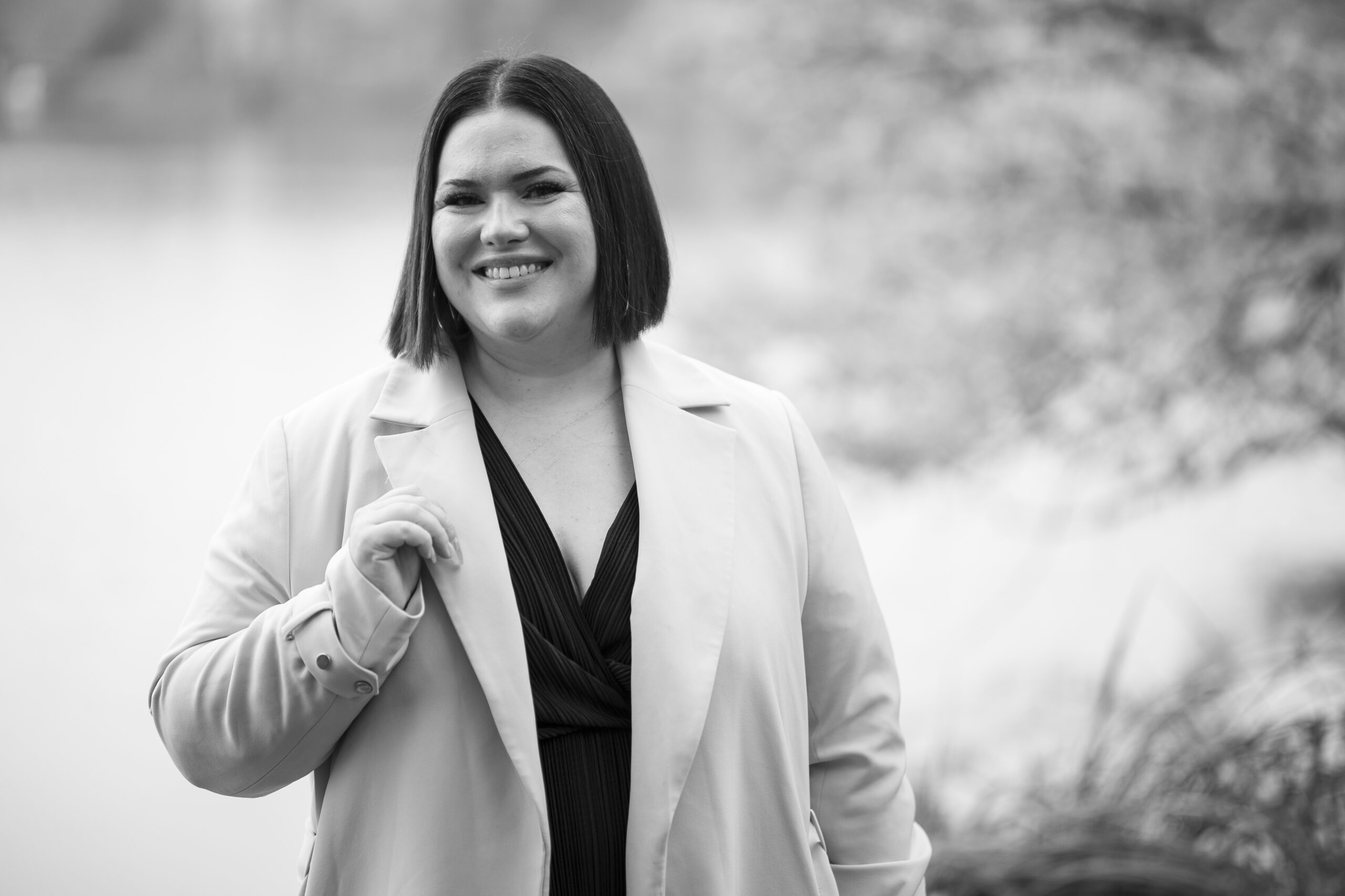 Frau sieht lächelnd in die Kamera, im Hintergrund ist ein Seeufer zu sehen